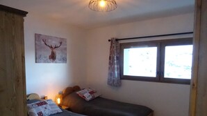 A room with two beds, a window with curtains, a wall-mounted light fixture, and a painting of a deer. - F101 - 40 m2 - 2P - 2/4 pers (Prapoutel)