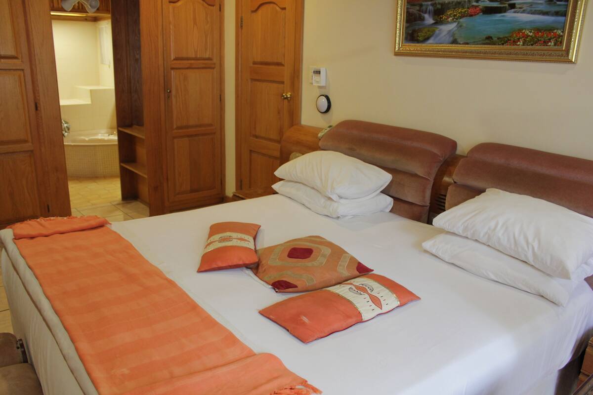 A hotel room with a bed, two wooden doors, a painting on the wall, and a bathroom visible through an open door.