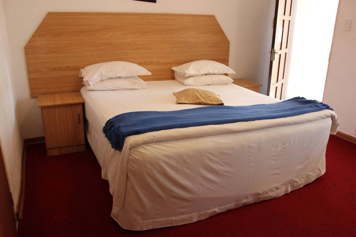 A bed with a wooden headboard, white bedding, and a blue blanket.