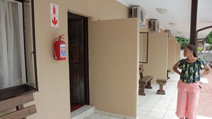 Entrada de hotel con extintor en la pared, señal de salida de incendios y un área de estar exterior cubierta con bancos.
