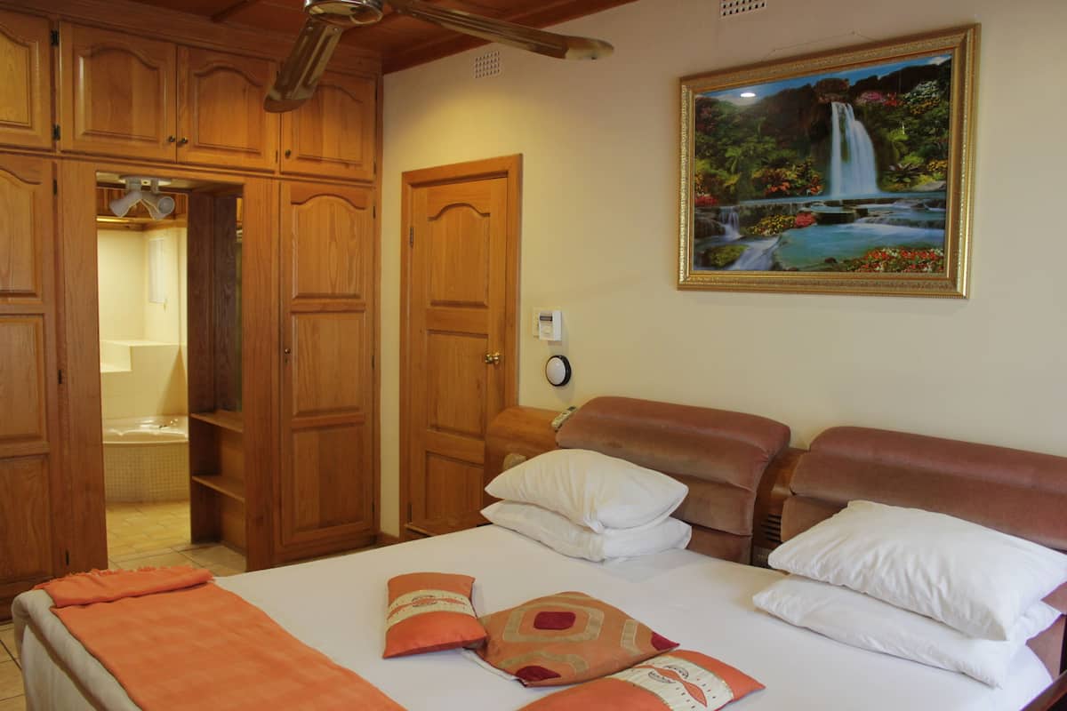 A hotel room with a bed, wooden wardrobe, and a painting of a waterfall.