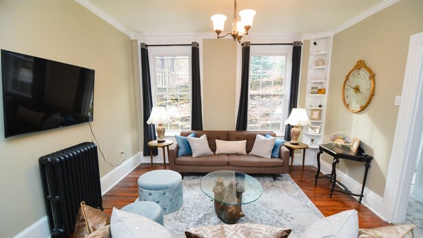 A living room with a brown sofa, a glass coffee table, and a television. - Däs Barenhaus on Broadway (4 Master Bedrooms) (Jim Thorpe)