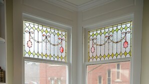 A dining room with a table set for four, two chairs, and a view of a red brick building through stained glass windows. - Däs Barenhaus on Broadway (4 Master Bedrooms) (Jim Thorpe)