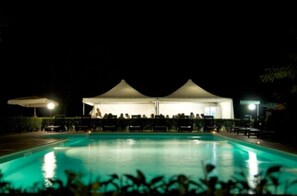 A nighttime swimming pool area with two white tents and lounge chairs. - Agriturismo Greppi (Crescentino)