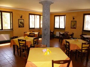 A dining area with multiple tables and chairs, a central column, and windows with blinds. - Agriturismo Greppi (Crescentino)