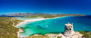 A coastal landscape with a clear turquoise sea, a sandy beach, and a historic stone tower.