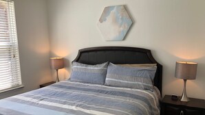 Un lit avec une couvre-lit à rayures, deux lampes de chevet, une horloge et une œuvre d’art abstraite accrochée au mur.