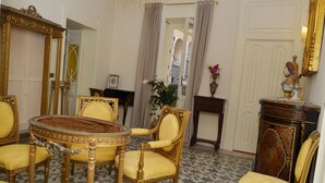 A room with a round table surrounded by ornate chairs, a large mirror, and a decorative fireplace. - "B&B" Casa D'Alleri "Quadruple room in a historic home in" Ortigia " (Siracusa)