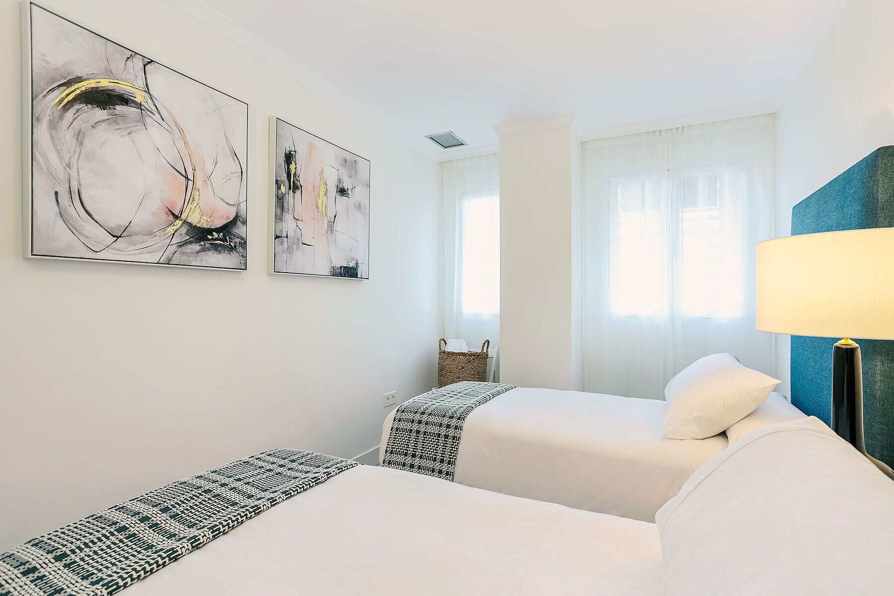 Hotellihuone, jossa on kaksi sänkyä, suuri ikkuna, jossa on verhot, ja seinällä on abstraktia taidetta.