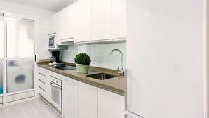 Una cocina moderna con armarios blancos, un lavamanos de acero inoxidable, una cafetera y una planta en maceta.