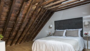 A bedroom with a sloped ceiling, a large bed with a grey headboard, two bedside lamps, and a small bedside table with a vase of flowers. - Genteel Home Trinidad Grund F (Málaga)