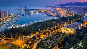 A coastal cityscape at dusk with a prominent bridge, marina, and urban buildings. - Genteel Home Trinidad Grund F (Málaga)