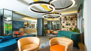 A modern lobby with sofas, a reception desk, and a bookshelf with plants. - Hampton by Hilton London Park Royal (London)