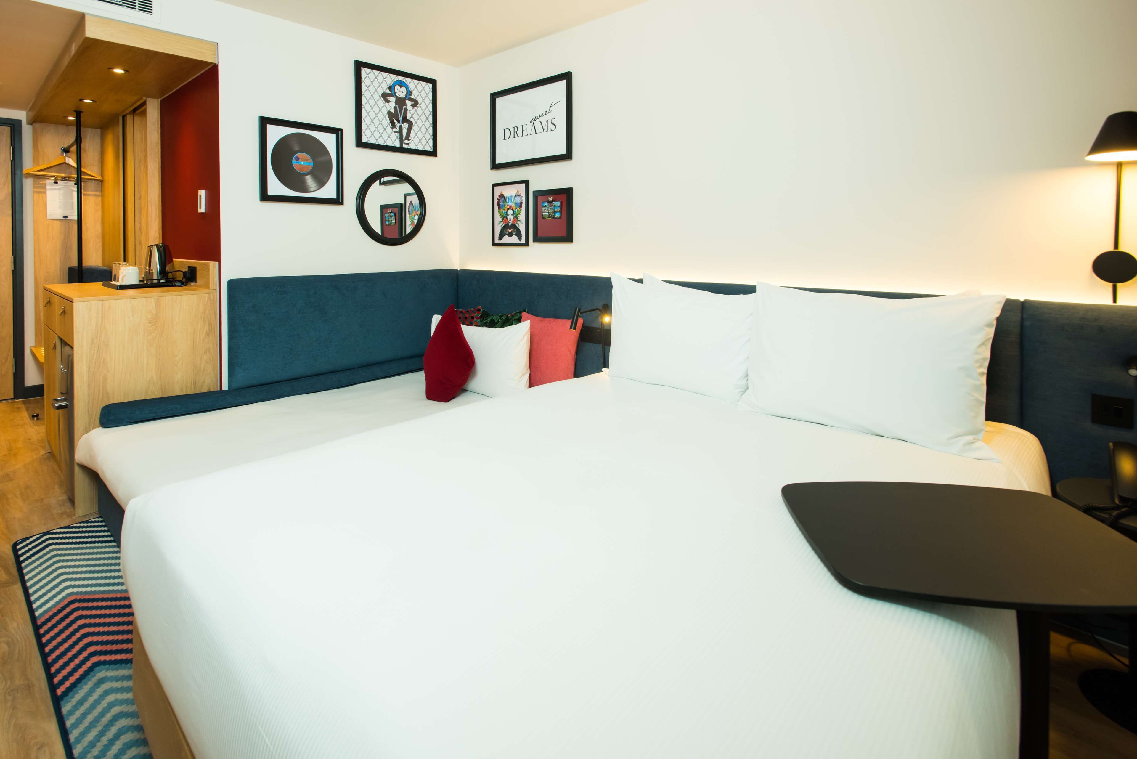 Quarto de hotel com uma cama grande, uma escrivaninha com cadeira e uma kitchenette pequena.