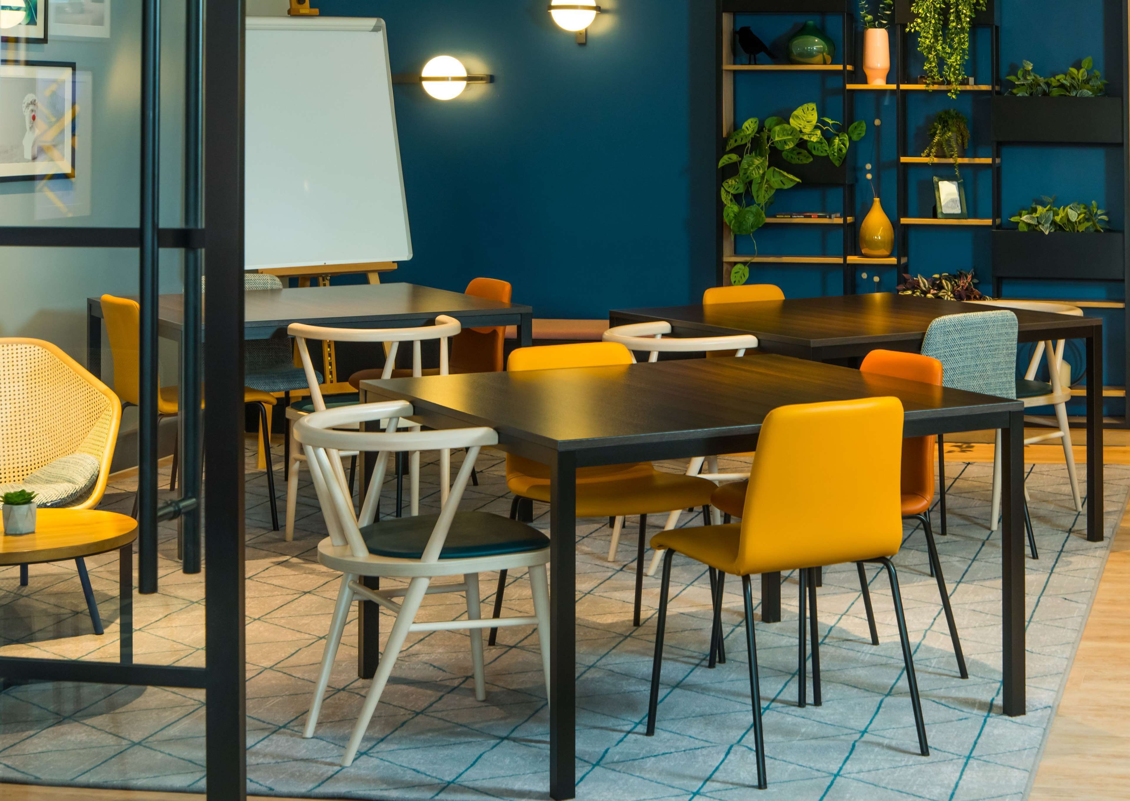 Un salón de conferencias con una mesa grande, sillas, una pizarra y estanterías con plantas.