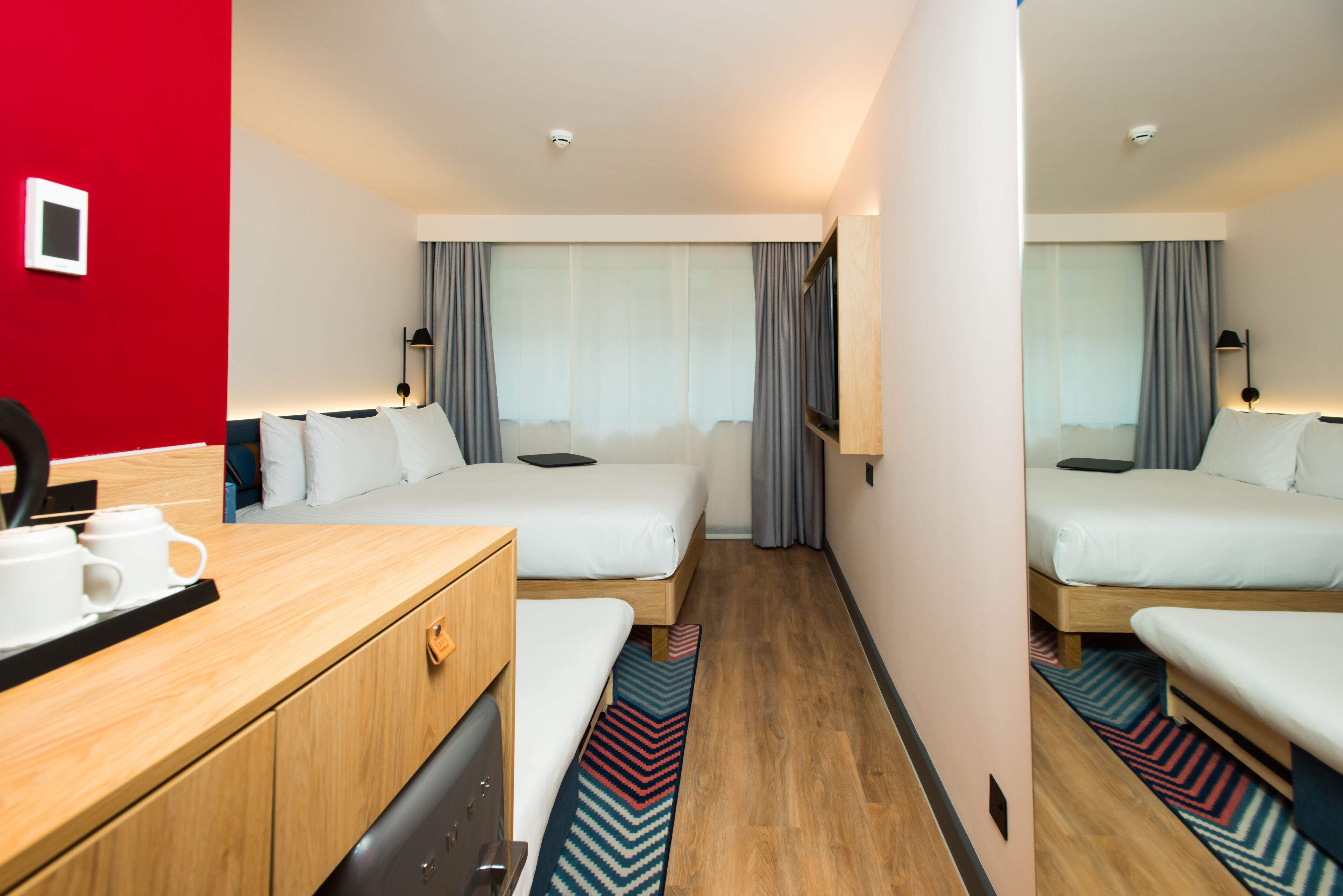 A hotel room with two beds, a wooden desk, a coffee station, and a view of the hallway.
