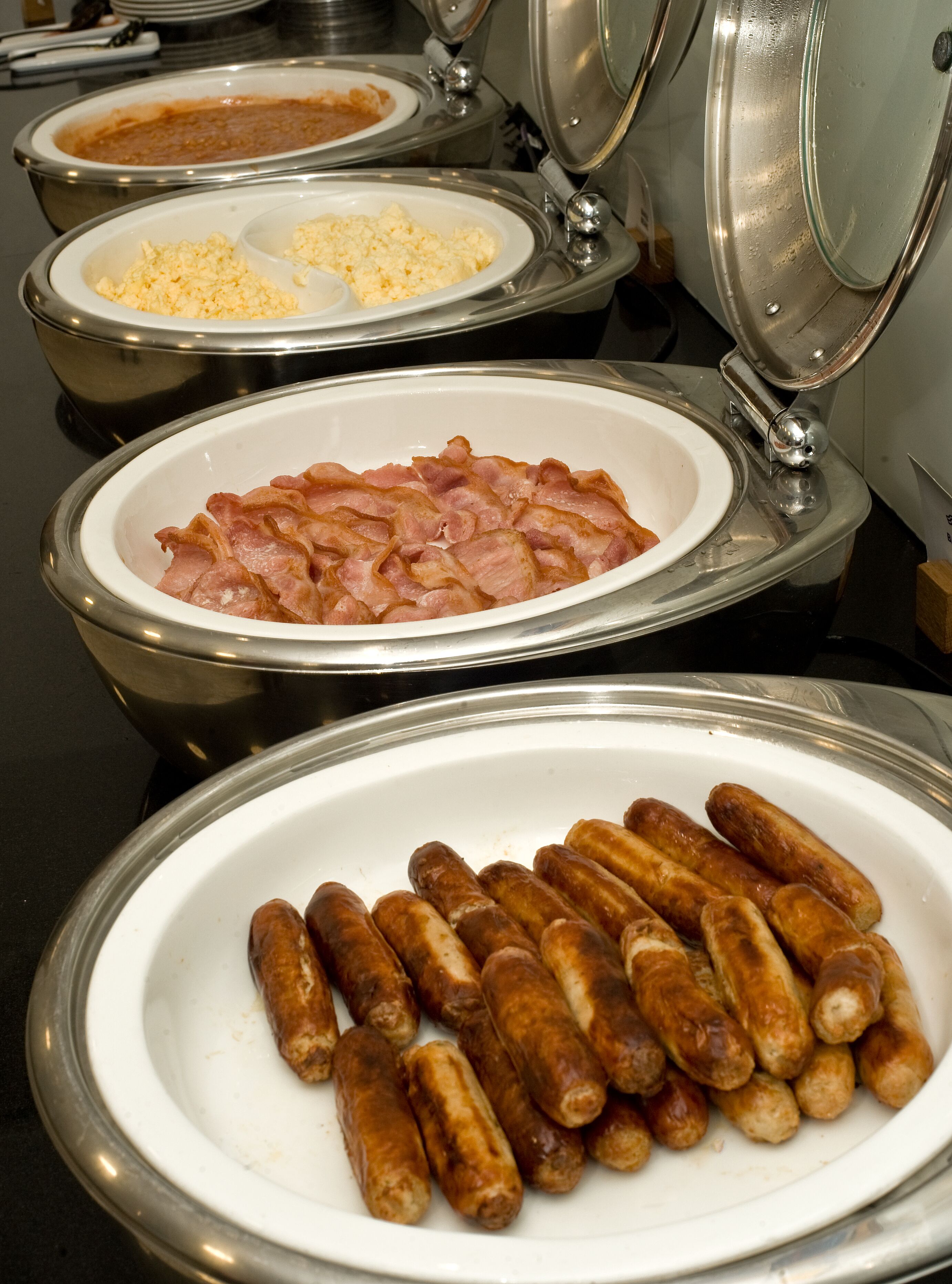 Un buffet proposant une variété de plats, notamment des saucisses, des œufs brouillés et du bacon.