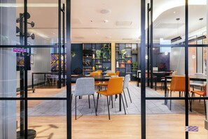 A modern interior with glass partitions, wooden flooring, and orange chairs around tables. - Hampton by Hilton London Park Royal (London)