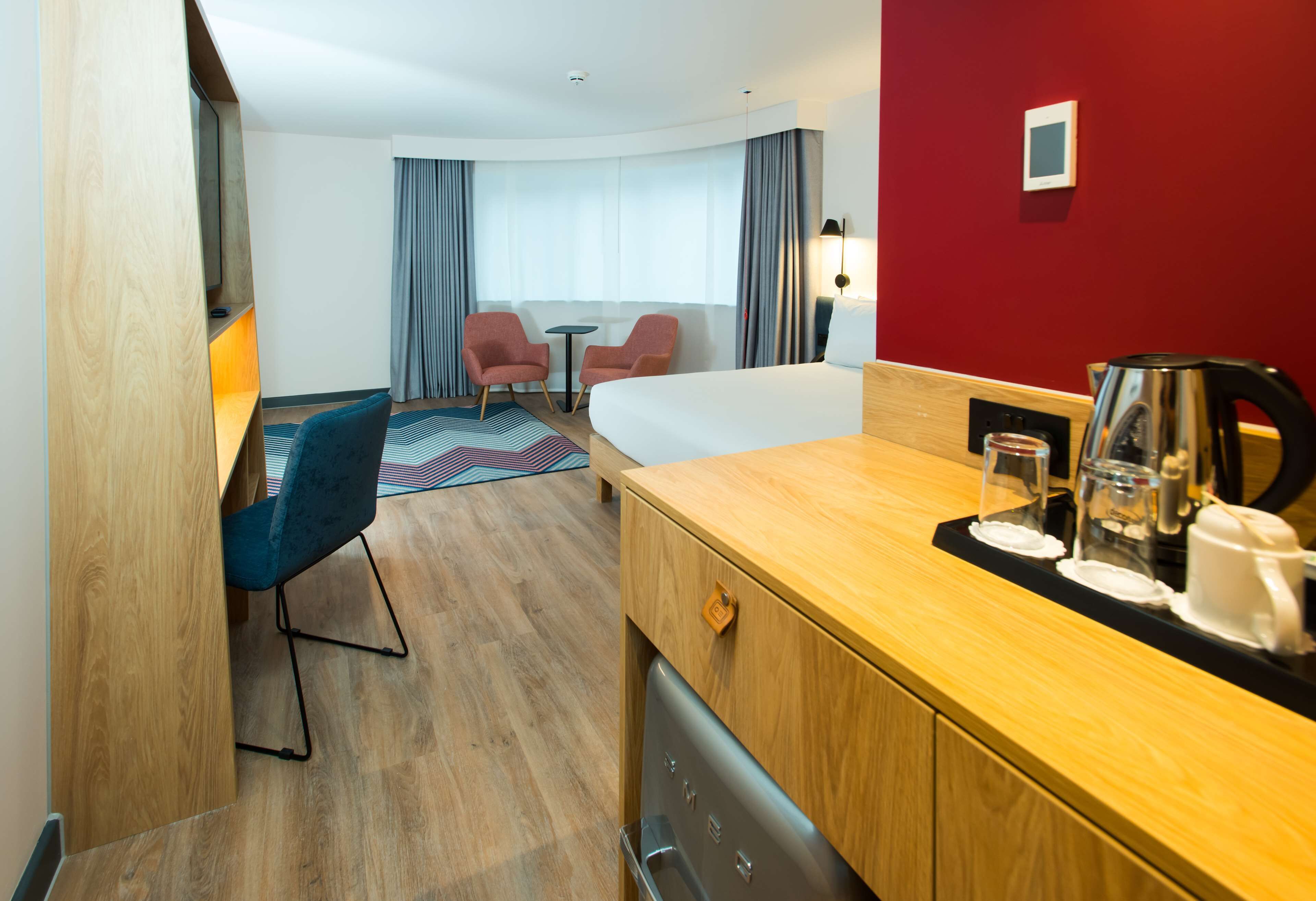 Een hotelkamer met een houten bureau, twee stoelen, een bed, een koffiezetapparaat en een kleine tafel.