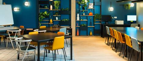 A modern meeting room with a long table, yellow chairs, and a blue wall with shelves of plants.