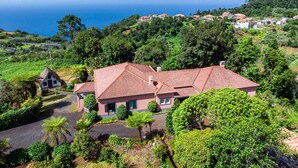 Una casa costera con techo de tejas rojas, rodeada de abundante vegetación y vista al mar.