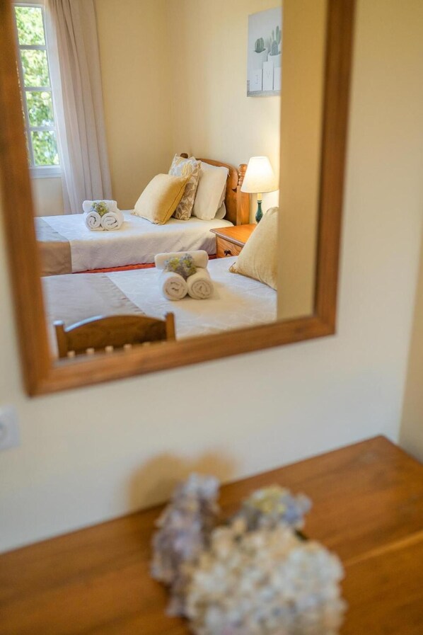 A hotel room with two beds, a wooden headboard, a bedside table with a lamp, and a mirror reflecting the room.