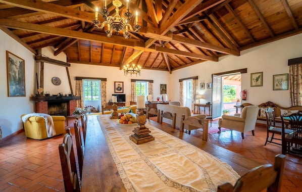 A spacious dining area with a long wooden table, chairs, and a chandelier. - Casa da Tia Clementina (Santana)