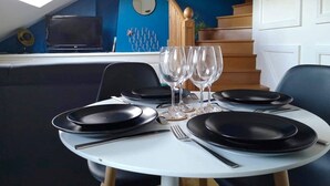 Ruokapöytä on katettu mustilla lautasilla, viinilaseilla ja aterimilla. Huoneessa on siniset seinät ja portaikko.
