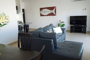 Un salon moderne avec un canapé, un pouf et un téléviseur à écran plat.