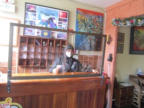 Une personne se tient derrière un comptoir, avec un miroir, une étagère remplie d’objets et un mur orné de tableaux.