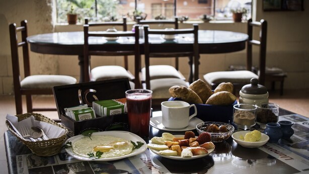 A breakfast setting with a table, chairs, and various breakfast items including eggs, pastries, and beverages. - Hosteria Llanovientos (Baños de Agua Santa)
