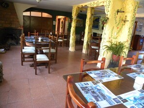 Un espace repas avec des tables et des chaises en bois, une cheminée et un mur végétal agrémenté d’un tableau.