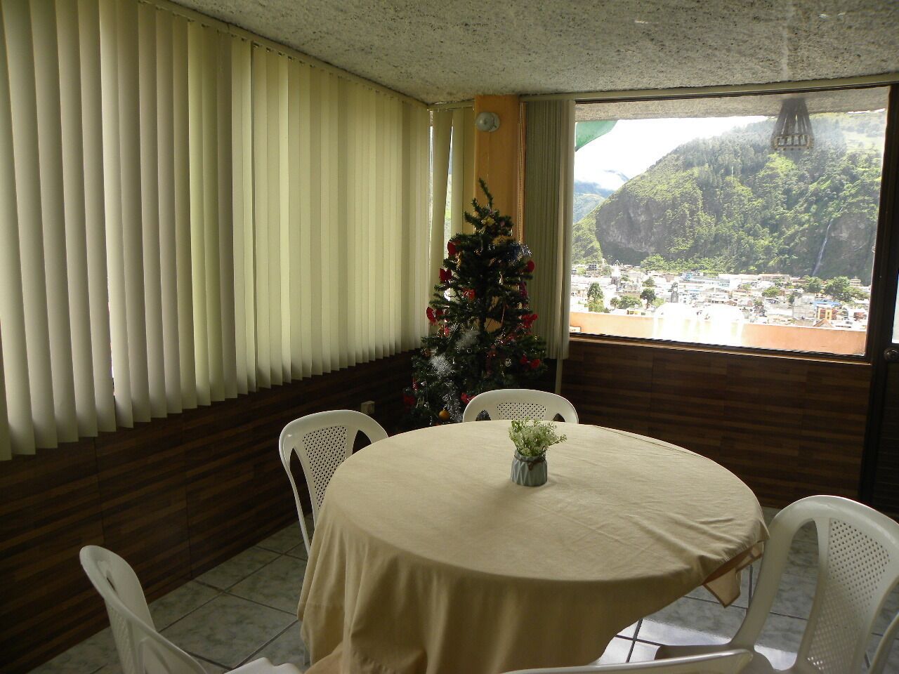Een eethoek met een ronde tafel, witte stoelen, een kerstboom en uitzicht op een bergachtig landschap door grote ramen.