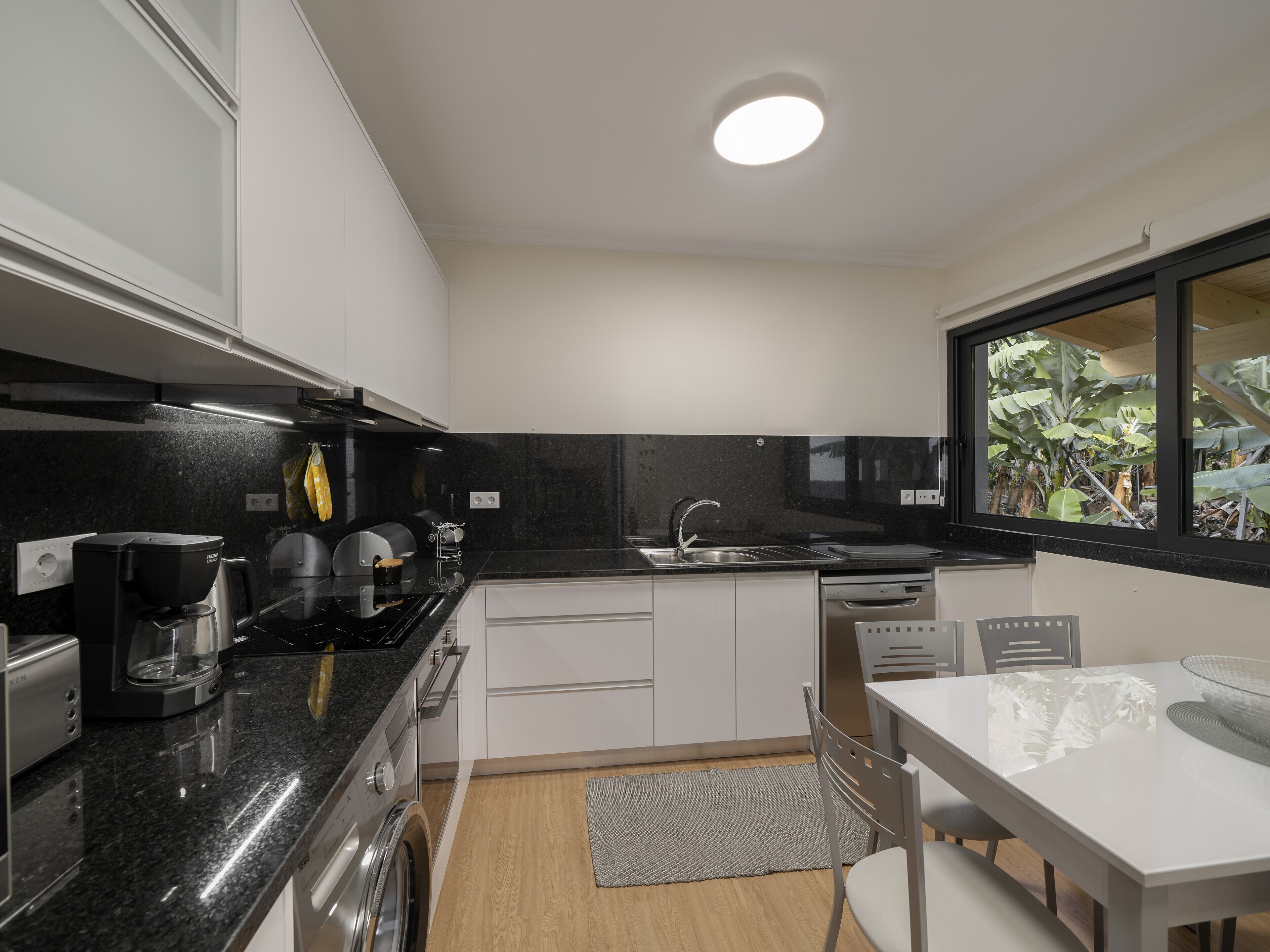 A modern kitchen with a black countertop, white cabinets, a built-in oven, and a window with a view of greenery.