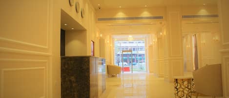 A hotel lobby with a reception desk, seating area, and a view of the street through the glass doors.