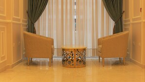 A hotel lobby with a patterned floor, two armchairs, a small table, and a large window with sheer curtains. - New MerryLand Hotel (Amman)