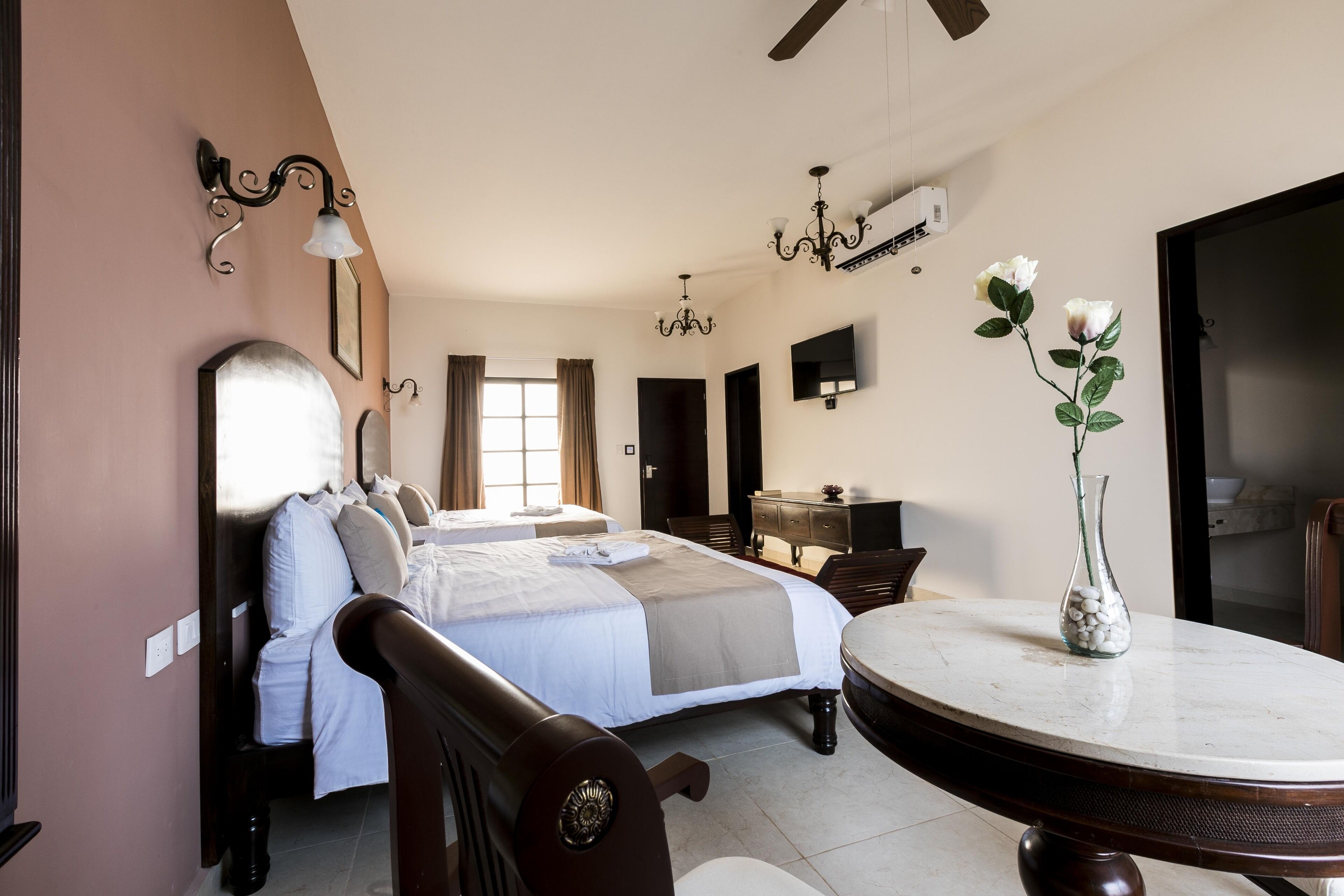 Une chambre d’hôtel avec un grand lit, une table ronde, un vase rempli de fleurs et un téléviseur fixé au mur.
