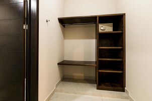 Um armário pequeno e escuro de madeira, com uma única prateleira e barra para pendurar roupas, localizado num canto de um quarto com paredes brancas e chão de azulejos.