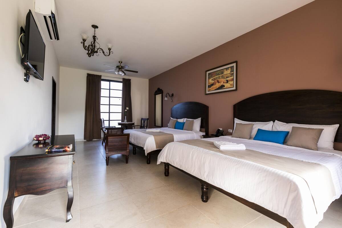 A hotel room with two beds, a TV, a chandelier, and a painting on the wall.