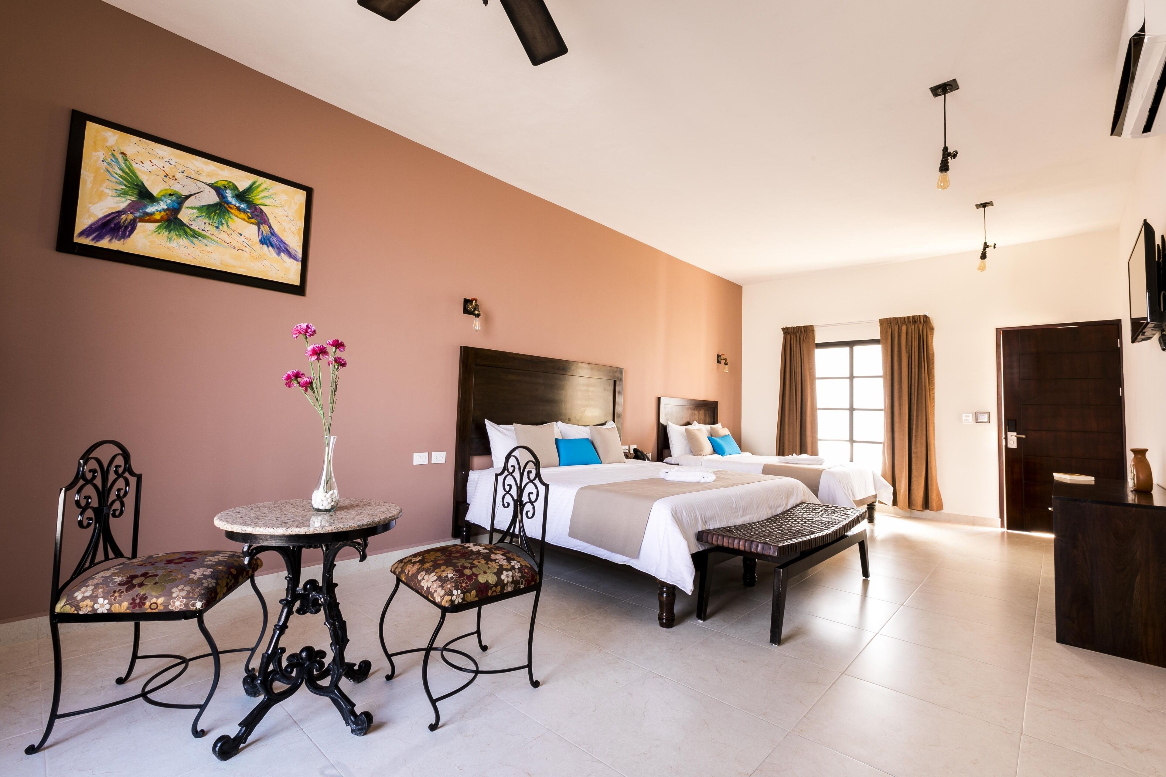A hotel room with a bed, a small round table with chairs, a decorative vase, and a painting on the wall.