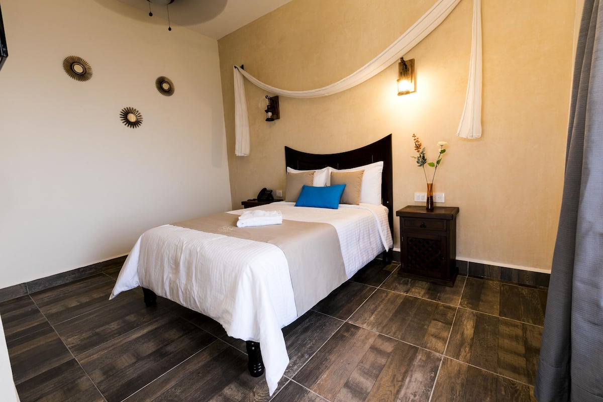 A neatly arranged bedroom with a large bed, a bedside table, a nightstand, and a wall-mounted light fixture.