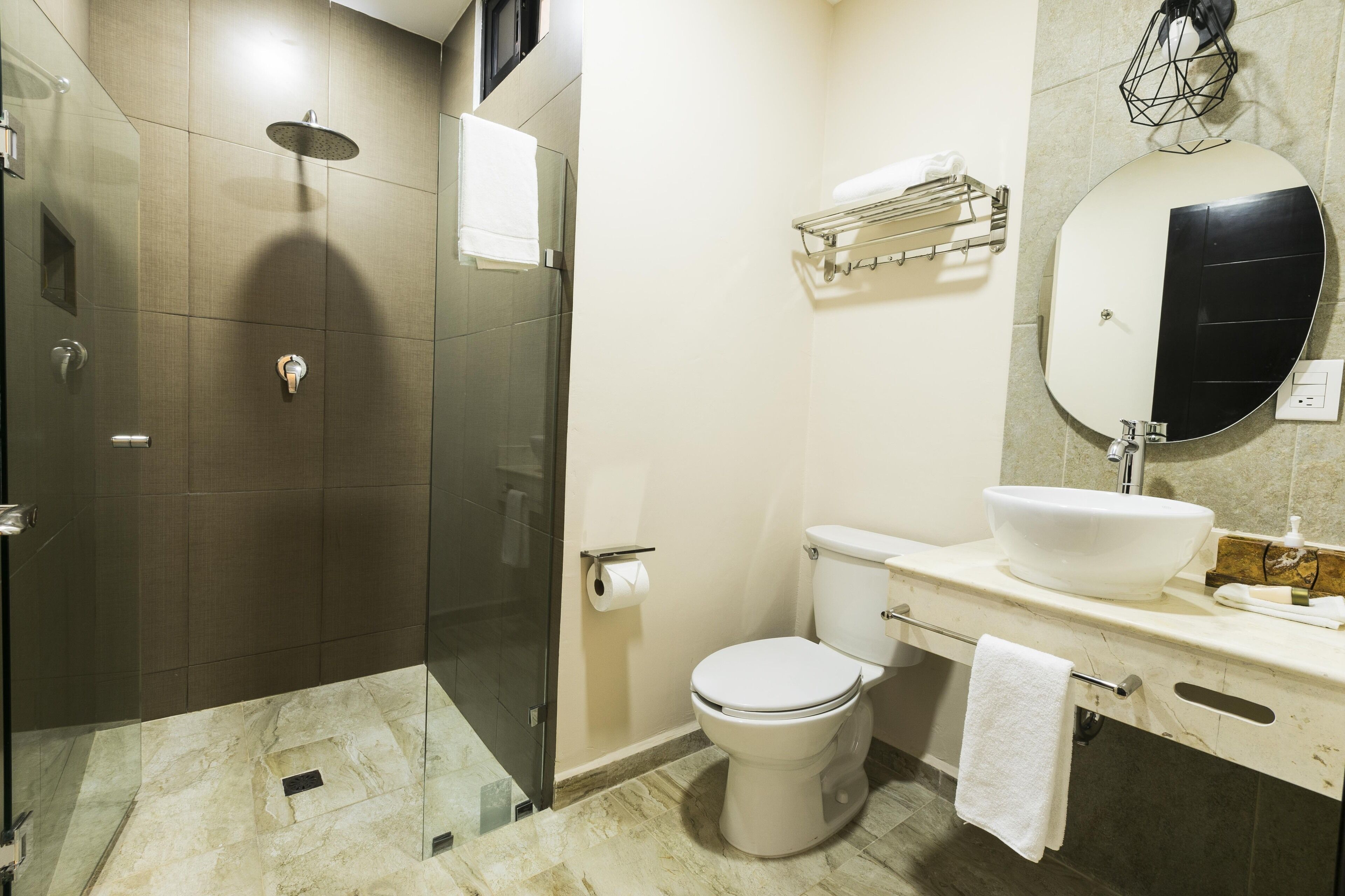 A modern bathroom with a glass-enclosed shower, a white toilet, and a large round mirror.