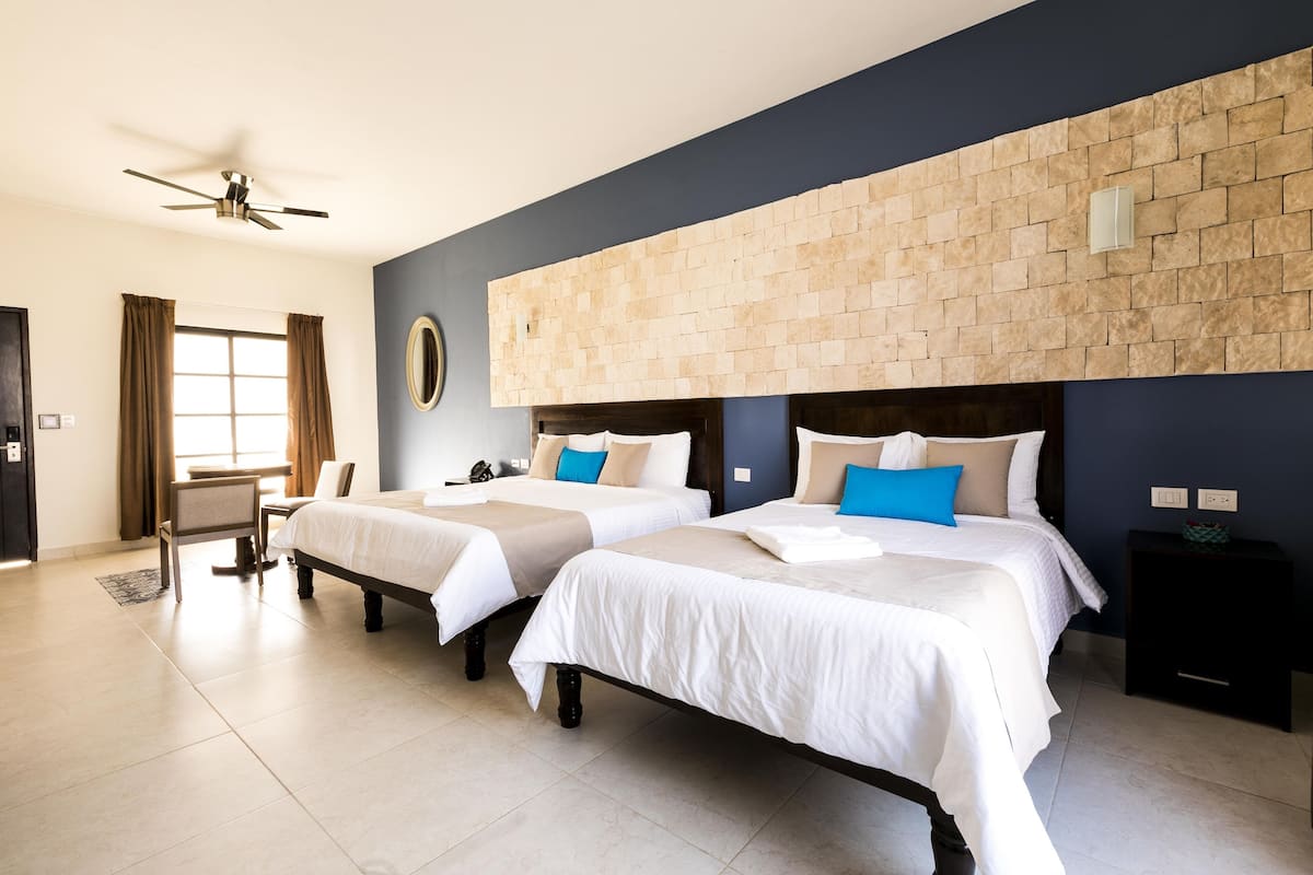 A hotel room with two beds, a desk, a chair, a ceiling fan, and a stone accent wall.