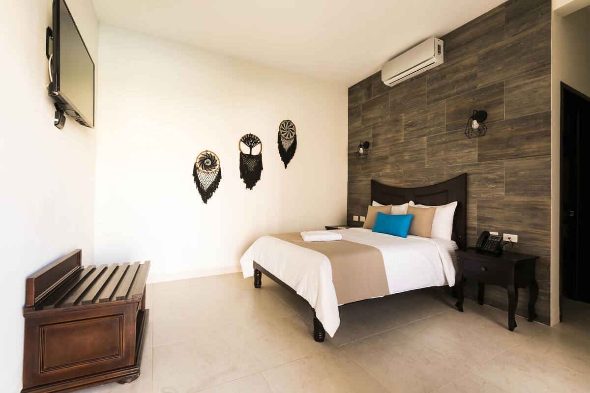 A hotel room with a bed, bedside tables, a TV, and wall-mounted air conditioning.