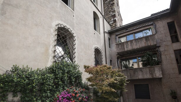 Une cour intérieure avec un bâtiment doté de fenêtres en arc de cercle et d’une façade en pierre.