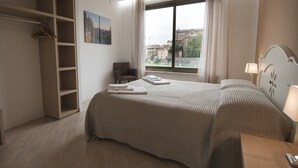 Une chambre d’hôtel avec un lit, une chaise, un bureau, une armoire et une fenêtre donnant sur des immeubles.