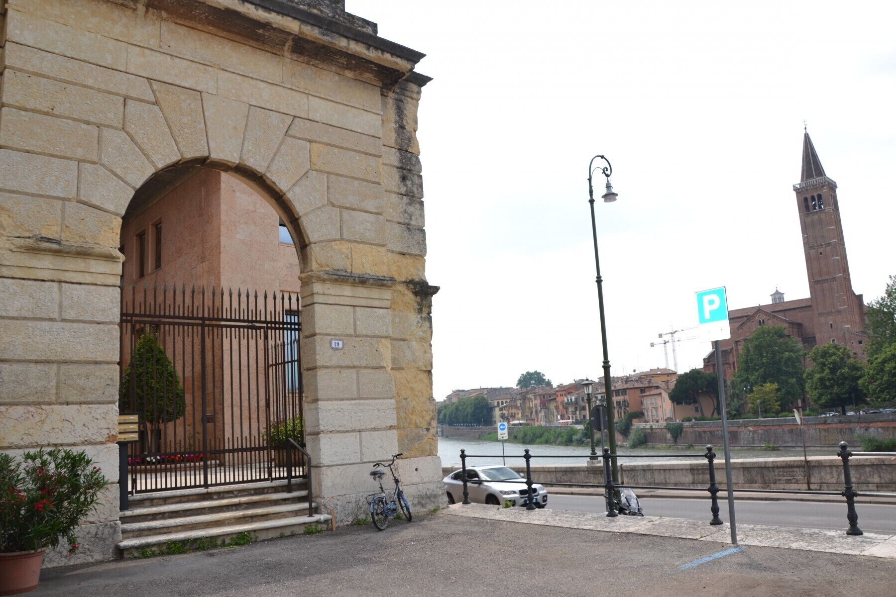 A stone building with a large arched entrance, a bicycle parked outside, and a car parked on the street.