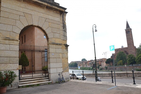 A stone building with a large arched entrance, a bicycle parked outside, and a car parked on the street.