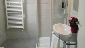 A modern bathroom with a glass shower enclosure, a white sink, and a towel rack. - AdagioRooms (Elmas)