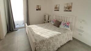 A bedroom with a bed, a window with curtains, a hanging lamp, and wall-mounted shelves. - AdagioRooms (Elmas)